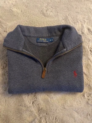 Blå halvzip tröja från Polo Ralph Lauren - Snygg blå half-zip tröja från Polo Ralph Lauren, klassisk röd logga på bröstet. Perfekt för en avslappnad men stilren look. Postar inom 24h!📦