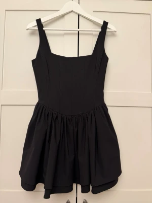 Svart kort klänning med volangkjol - Perfect little black dress! Korsett som snappar åt midjan.  Helt ny med prislapp kvar! 
