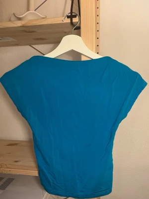 Blå croppad topp med öppen rygg - Snygg blå croppad topp med öppen rygg och korta ärmar. Toppen har en enkel, stilren design och är tillverkad i ett mjukt bomullsliknande material. Perfekt att matcha med höga jeans eller kjol.