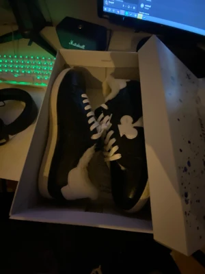 Gallerist skor  - Säljer ett par svarta sneakers med vit sula och vita snören. Skorna har en stor vit detalj på sidan och är fodrade med mjukt fårskinn för extra komfort. Perfekta för dig som vill ha något unikt och varmt till vardagslooken.