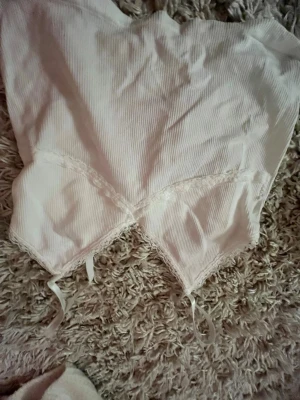 Vit ribbad linne med smala band - Söt vit linne med ribbad struktur och spetsdetaljer längs bysten. Smala axelband och dekorativa band framtill. Perfekt för dig som gillar en romantisk och feminin stil. Materialet känns mjukt och stretchigt.