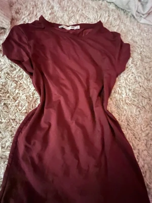 Vinröd t-shirt från 157 - Säljer en enkel och stilren vinröd t-shirt från 157. T-shirten har korta ärmar och en klassisk rund halsringning. Tillverkad i mjukt bomullsmaterial som känns skönt mot huden. Perfekt basplagg att matcha med jeans eller kjol. Supersnygg på allt och alla! Storleken är M men känns som typ S!