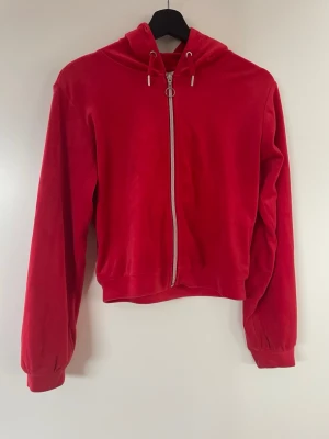 Röd hoodie med dragkedja från Gina Tricot - Snygg röd hoodie från Gina Tricot med dragkedja framtill och rund metallring som zip puller. Hoodien har huva med dragsko och långa ärmar. Tillverkad i mjukt, skönt material som känns riktigt chill. Perfekt för dig som gillar en enkel men ändå statement look.