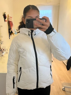 Vit dunjacka  - Snygg vit puffer dunjacka från McKinley med svarta dragkedjor och många fickor. Den är mycket varm och passar även perfekt som skidjacka. Går att knäppa i midjan och fästa vid händerna. 