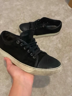 Svarta sneakers med vit sula - Stilrena svarta sneakers med lågt skaft och vit, platt sula. Skorna har snörning och detaljer i både mocka och skinn, samt rund tå. Passar perfekt till en avslappnad streetwear-look.