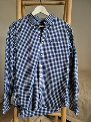 Blårutig skjorta från American Eagle, storlek M - Snygg blårutig skjorta från American Eagle med klassisk button-down krage och bröstficka. Skjortan har vita knappar. 100% bomull, storlek M.