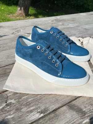 LANVIN - Extremt exklusiva och sällsynt färg på dessa snygga blå sneakers från Lanvin med ovandel i mocka och detaljer i blankt lack. Riktigt mäktiga att bära och så gott som nya🙌 Om du har några frågor så är det bara att skriva. Storlek : uk 6 / 41. Köpta på Care Of Carl. Nypris 5200