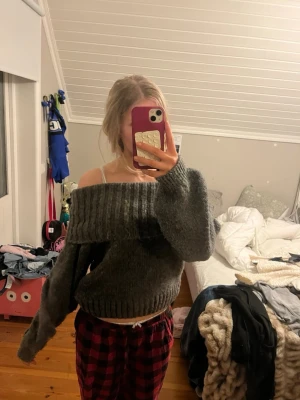 Mörkgrå off shoulder stickad tröja - Säljer en mörkgrå stickad tröja med bred off shoulder-krage och ballongärmar. Tröjan har ribbstickade muddar vid ärmslut och nederkant. Perfekt för dig som vill ha en trendig och mysig look till hösten eller vintern.