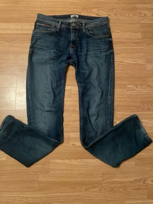 Blå jeans från Hilfiger Denim - Säljer ett par klassiska blå jeans från Hilfiger Denim i storlek 33/34. Jeansen har en rak passform, fem fickor och snygga kontrastsömmar. Perfekta till vardags och passar till det mesta. Materialet är slitstarkt denim i bomull. På första bilden så är den en fläck på högerbenet,går att tvätta bort, bara tandkräm sen kanske någon liten till men sist så är de två olje fläckar som inte riktigt ger sig, går säkert att få bort med mer ork. Pris går att diskutera!