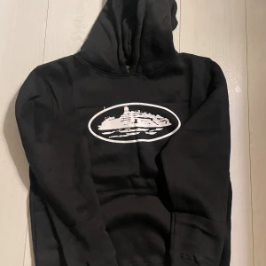 Svart hoodie med tryck - Svart hoodie från Visby med ett vitt tryck av alcatraz på bröstet. Tröjan har huva, lång ärm och en klassisk känguruficka framtill. Materialet är mjuk bomull och passformen är normal. Perfekt för dig som gillar stilrena och bekväma plagg.