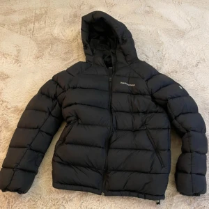 Svart dunjacka Peak Performance M - Svart dunjacka från Peak Performance (använd 1-2ggr) med huva och dragkedja. Perfekt för kalla dagar och har en clean, sportig look. Broderad logga på bröstet.                     Hör av er vid fler frågor!
