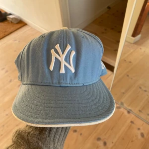 Blå New Era Yankees keps - Snygg ljusblå keps från New Era med klassisk New York Yankees-logga broderad i vitt framtill. Kepsen har böjd skärm och vit kant runt om, samt New Era-logga på sidan. Perfekt för dig som vill ha sportig streetstyle.