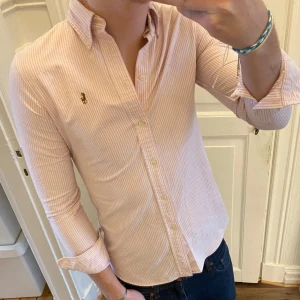 Rosa och vit randig skjorta från Ralph Lauren - Snygg rosa och vit randig skjorta från Ralph Lauren med broderad logga på bröstet. Skjortan har en klassisk krage. 