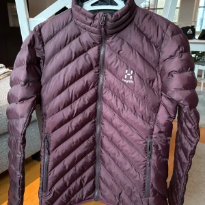 Base mimic jacket W, isoleringsjacka dam Haglöfs - Säljer en snygg vinröd dunjacka från Haglöfs med quiltad design. Jackan har två praktiska fickor med dragkedja. Den är aldrig använd!