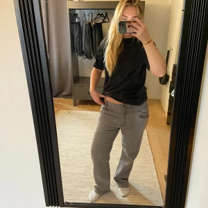 Grå randiga straight byxor - Säljer ett par grå byxor med tunna vita ränder och raka ben. Byxorna har låg midja och klassisk femficksdesign med dragkedja vid ena fickan. Snyggt avslappnad passform och passar perfekt till en chill vardagslook.
