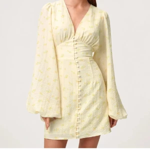 Adoore blommig gul klänning - Supersöt ljusgul klänning från Adoore med små gula blommor, v-ringning och klädda knappar framtill. Klänningen är använd 2 gånger så är fortfarande i toppen skick. 