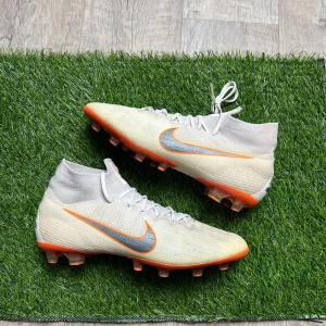 Nike Mercurial Superfly fotbollsskor 44 - Snygga Nike Mercurial Superfly fotbollsskor i ljusgrått med orange och silver detaljer. Skorna har snörning, hög krage och platt sula med dobbar för bra grepp på planen. Ovandelen är i Flyknit-material för en tight passform och lätt känsla.