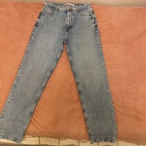Blå raka jeans från Zara, strl 36 - Snygga ljusblå jeans från Zara i klassisk rak modell med fem fickor och knappstängning. Jeansen har hög midja och är tillverkade i jeansmaterial med en normal passform. Perfekta för en chill och stilren look.