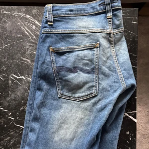 Nudie jeans grim tim W33 L32 - Säljer mina sjukt snygga Nudie Jeans! De har en riktigt fin och unik tvätt som inte längre säljs, vilket gör dem ganska sällsynta – därav priset.  Jeansen har en liten defekt (se bild 5) – det fanns tidigare ett hål som jag har lagat med en lapp på insidan. Lagningen är diskret och syns knappt alls, och det finns alltså inget hål kvar.  ✅ Längd: 105 cm ✅ Midjemått: 44 cm  Skriv gärna om du har frågor 