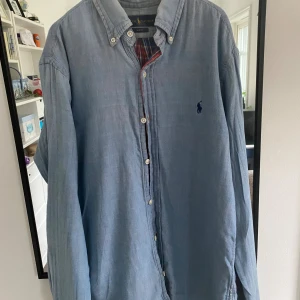 Blå skjorta från Ralph Lauren Slim Fit - Snygg ljusblå skjorta från Ralph Lauren i slim fit-modell. Skjortan har klassisk krage, knappar hela vägen och det ikoniska broderade Polo-logot på bröstet. Priset är inte fast så de gårno diskutera vid en snabb affär.