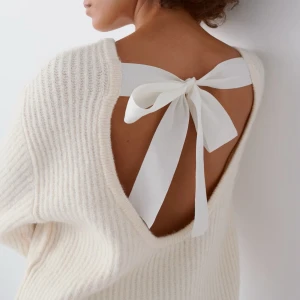 Vit stickad tröja med rosett i ryggen - Superfin vit stickad tröja med öppen rygg och stor rosett i vitt band. Tröjan har långärmade, lite breda ärmar och en mjuk, ribbad struktur. Perfekt för dig som gillar unika detaljer och vill ha en mysig men stilren look. Bara använd någon enstaka gång, skriv privat för frågor eller egna bilder 💓