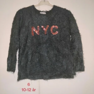 Grön fluffig tröja med rosa paljetter - Supermjuk och fluffig grön tröja med paljettbokstäver i rosa  'NYC' på bröstet. Varma tröjor nu till vintern. Fluffig tröja för flickor strl 10-12 år