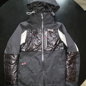 Svart pufferjacka från 8848 Altitude - Snygg svart pufferjacka från 8848 Altitude med glansiga paneler och vita detaljer på ärmarna. Jackan har huva med snörning, hel dragkedja och praktiska fickor. Perfekt för kalla dagar och har en cool sportig look.