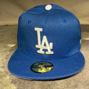 Blå LA Dodgers keps från New Era - Säljer en blå LA Dodgers 59FIFTY keps från New Era. Passar inte så behövdes inte😁. Klassisk modell med platt skärm, broderad LA-logga framtill och MLB-logga bak.  Kepsen är i bomull och har vita detaljer samt New Era-logga på sidan. Perfekt för dig som gillar sportig streetstyle.