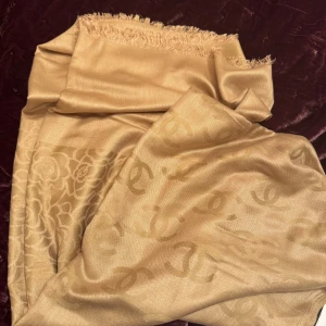 Guldaktig/Champagnefärgad halsduk i silke cashmere - Superfint skick. Syns knappt att den använts. Lyxig och mjuk halsduk i guld/champagnefärgad ton med blommönster. Materialet är silke/Cashmere i ganska tunt material, och har en elegant glans. Värmer gott nu på hösten/vintern. Fransen längs kanten ger en chill vibe och halsduken är stor nog att svepa runt halsen eller axlarna. Glömde att jag hade  köpt en liknande i annat märke i våras. Så man fick välja vilken som skulle säljas. Men helt underbar. Skickar direkt när betalning skickats. 
