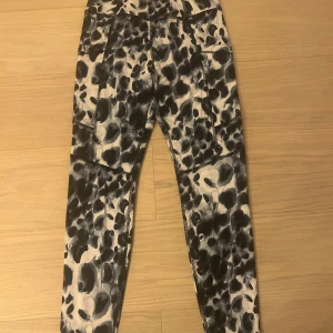 Svarta och vita leopardmönstrade leggings från SOC - Snygga fodrade leggings från SOC med svart och vit leopardmönster. De har praktiska fickor på sidorna och är tillverkade i ett stretchigt syntetmaterial som andas. Perfekta för träning och har en tight passform med hög midja.