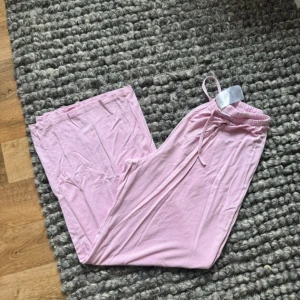 Ljusrosa mjukisbyxor från Ginatricot XS - Säljer ett par ljusrosa mjukisbyxor från Ginatricot i storlek XS. Byxorna har en loose passform med breda ben, elastisk midja och snörning framtill. Mjukt bomullsmaterial som är skönt mot huden. Perfekta för chill dagar hemma.