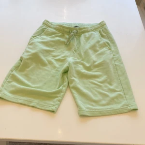 Mintgröna shorts med snörning - Fräscha mintgröna shorts från Kappahl i mjuk bomull. De har elastisk midja med snörning, två sidofickor och en diskret logga vid benet. Perfekta för chill dagar och sommarhäng. Passformen är normal och materialet är riktigt skönt mot huden.