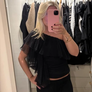 Svart oneshoulder volangtop - Säljer en svart oneshoulder topp med stora volanger och plisserad mesh. Helt ny 