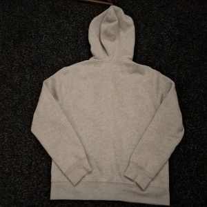 Grå hoodie från Polo Ralph Lauren - Snygg grå hoodie från Polo Ralph Lauren med dragkedja och huva. Tröjan har lång ärm, två fickor fram och den klassiska Polo-loggan broderad på bröstet. Perfekt för chill dagar och enkel att matcha med jeans eller joggers.