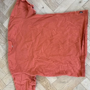 Orange Nike t-shirt i bomull - Säljer en orange t-shirt från Nike i storlek S. T-shirten har klassisk rund hals och korta ärmar, med en diskret Nike-logga broderad på bröstet. Materialet är mjuk bomull som känns skönt mot huden. Perfekt för dig som gillar sportiga och stilrena plagg.