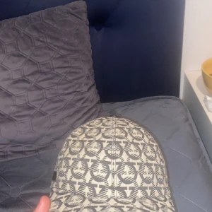 Beige och grå keps från Emporio Armani - Snygg keps från Emporio Armani i beige och grått med ett all-over logomönster. Klassisk böjd skärm och justerbar rem baktill. Perfekt accessoar för att lyfta din streetwear-look.