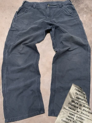 Vintage cargopants från Carhartt - Säljer ett par cargopants från Carhartt i 100% bomull. Byxorna har flera praktiska fickor, bred passform och klassisk Carhartt-logga på bakfickan. Perfekta för dig som gillar en avslappnad och funktionell stil.