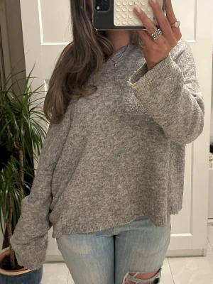 Grå oversized stickad tröja - Mysig grå stickad tröja med oversized passform och långa ärmar. Tröjan har en enkel, clean look och är perfekt för lager på lager. Mjuk och skön, passar till jeans för en chill vibe.