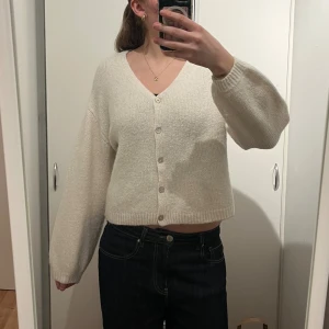 Vit kofta från Gina Tricot - Mysig vit kofta från Gina Tricot med v-ringning och stora knappar framtill. Perfekt att slänga på sig över ett linne eller t-shirt. Sitter lite som en S