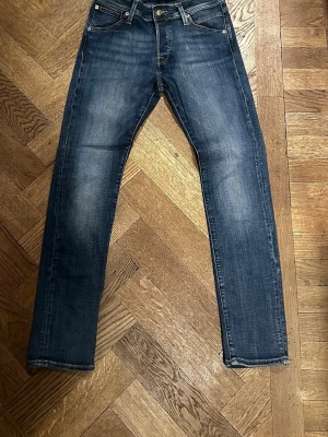 Slim Glenn blå jeans 28/30 - Snygga blå jeans från Slim Glenn i storlek 28/30. Modellen har en slim passform med klassisk femficksdesign och dragkedjegylf. Jeansen har en lätt tvättad look och raka ben som ger en clean och modern stil. Perfekta till sneakers eller boots.