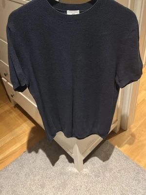 Mörkblå stickad tröja från H&M - En enkel och stilren mörkblå stickad tröja från H&M med regular fit. Tröjan har rund halsringning och korta ärmar, perfekt för dig som gillar en clean och klassisk look. Passar till det mesta och är superenkel att matcha.