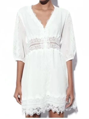 Vit spetsklänning från Zara - Superfin vit kortklänning från Zara med v-ringad hals och vackra spetsdetaljer längs kanter, midja och ärmar. Klänningen har puffiga kortärmar och är gjord i ett lätt material som känns luftigt. Perfekt för dig som gillar romantisk stil och snygga detaljer.