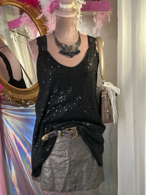 Glittrig svart paljett topp/ klänning med spetsband - tunika. Den har breda axelband i spets och är täckt av paljetter över hela plagget. Går utmärkt att bära som en kortare klänning eller som en topp (styla gärna med ett bälte i midjan!).  Sitter som en M/L Fantastisk skick inga paljetter saknas.