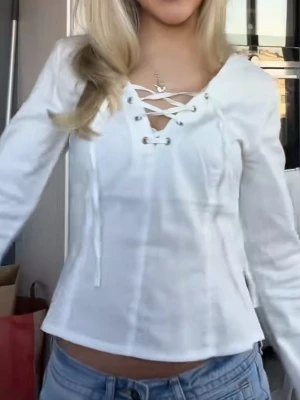 Vit långärmad topp med snörning - Säljer en vit långärmad topp med snygg snörning framtill och v-ringad hals. Toppen har en lätt figurnära passform och är tillverkad i ett mjukt tyg som känns skönt mot huden. Perfekt att styla med jeans eller kjol.