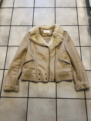 Beige pälsjacka från VILA, storlek L - Säljer en beige pälsjacka från VILA i storlek L. Jackan har mjukt fuskpälsfoder, bred krage och dragkedjor på fickorna. Snygga detaljer med knappar framtill och uppvikta ärmslut. Perfekt för kalla dagar och ger en cool look.