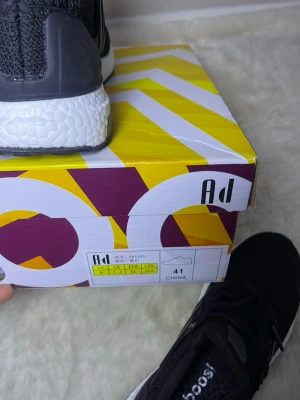 Svarta Adidas Ultraboost sneakers - Säljer ett par svarta Adidas Ultraboost sneakers i storlek 41. Skorna har en stickad ovandel i mesh, klassiska tre ränder på sidan och vit Boost-sula för extra komfort. Perfekta för dig som vill ha både stil och funktion. Snörning framtill.