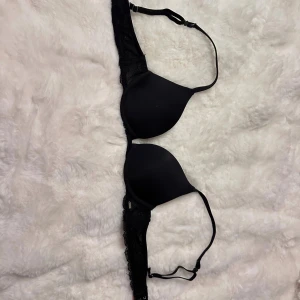 Svart push-up bh från Hunkemöller - Säljer en svart push-up bh från Hunkemöller i storlek 75AA. Bh:n har släta kupor och spetsdetaljer längs sidorna samt justerbara axelband för perfekt passform. Enkel och stilren design som funkar till allt.