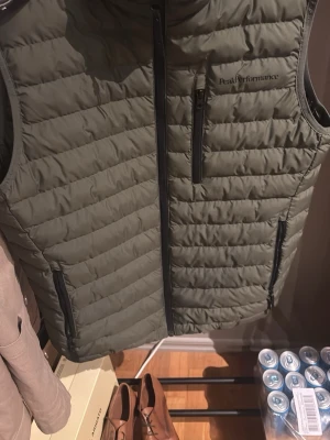 Olivgrön dunväst Peak Performance M - Säljer en olivgrön dunväst från Peak Performance i storlek M. Västen har quiltad design, hel dragkedja framtill och tre fickor med dragkedja. Perfekt för lager-på-lager och outdoor-vibe.