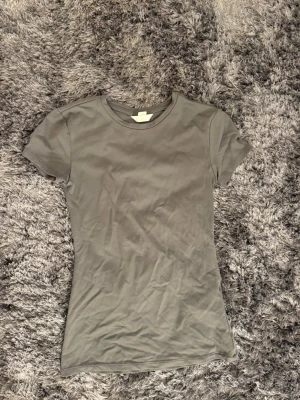 Grå basic t-shirt XS - En enkel grå t-shirt i slim fit med rund hals och korta ärmar. Perfekt att matcha med jeans eller kjol för en clean och stilren look. Tillverkad i mjuk bomull som känns skön mot huden.