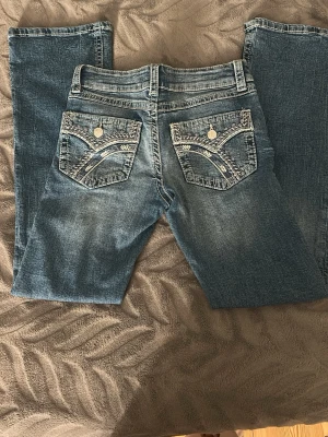 Blå jeans med broderade fickor Gina Tricot - Snygga blå jeans från Gina Tricot i storlek 152. Endast använda 1 gång. Jeansen är bootcut och coola broderade bakfickor med silvriga knappar. Klassisk denimlook med ljusare tvätt och detaljerade sömmar. Perfekta för dig som vill sticka ut lite extra.